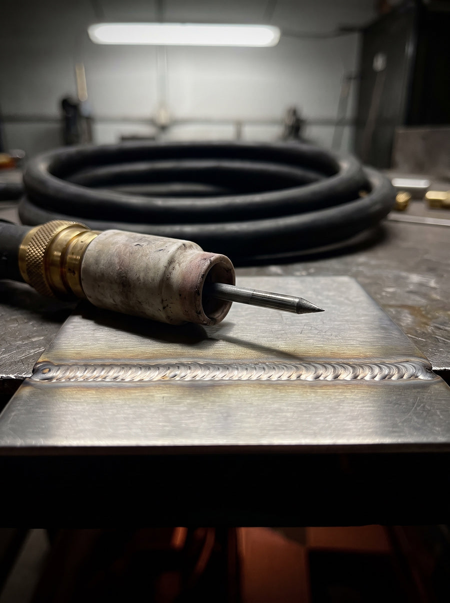 The TIG Field Card cover, a TIG torch resting on a plate beside a finished bead