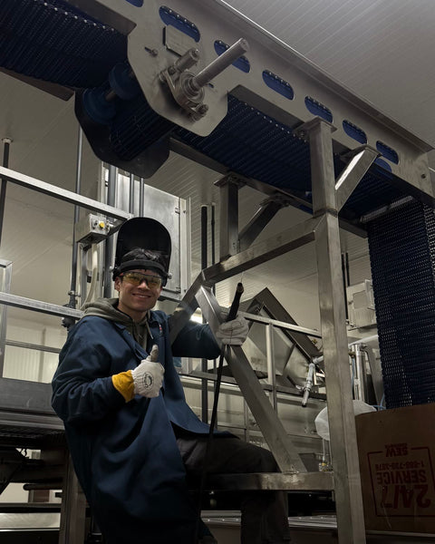 Dakota on a conveyor frame in a food plant, hood flipped up, TIG torch in hand
