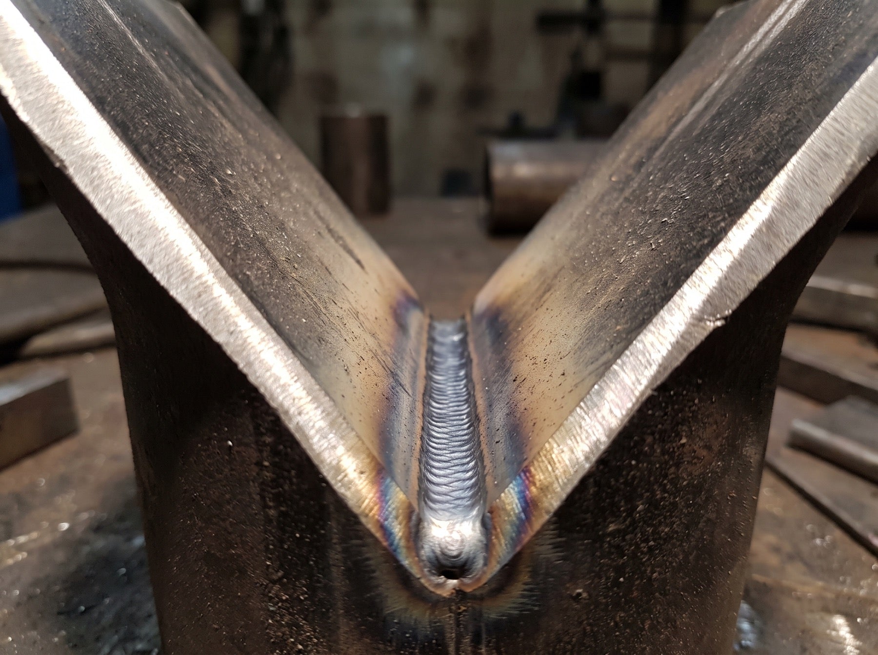 Macro of a root pass laid in the bottom of an open V groove between two beveled pipe sections, the bevel still unfilled above it